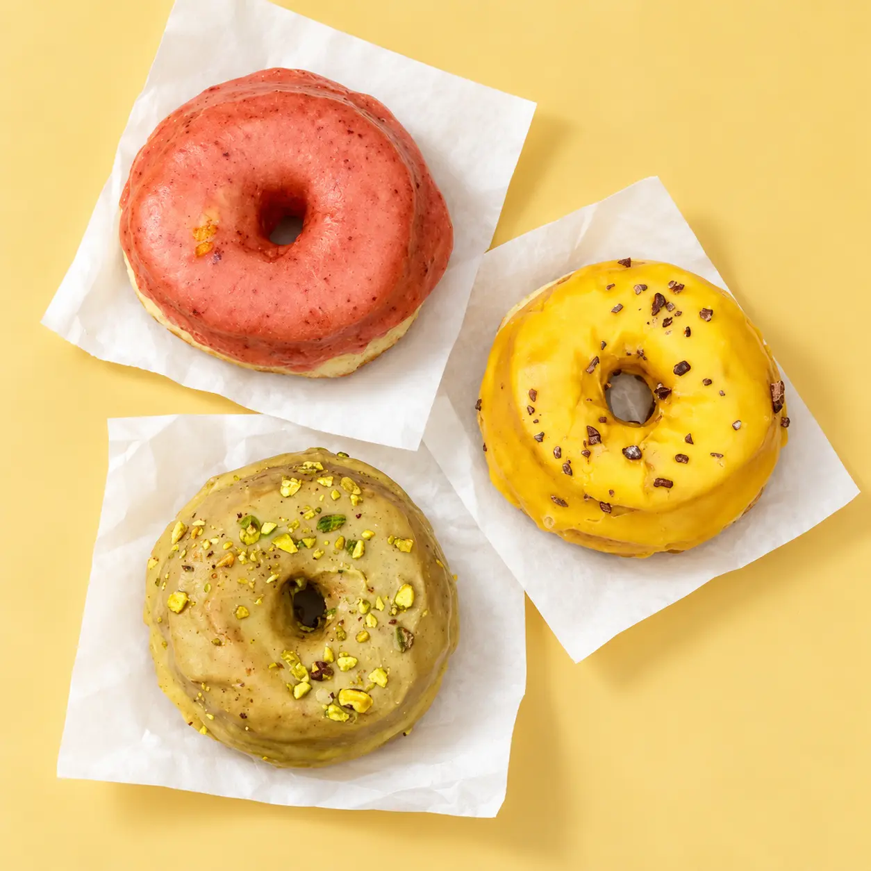 Three Gracie’s donuts on white paper and a yellow tabletop
